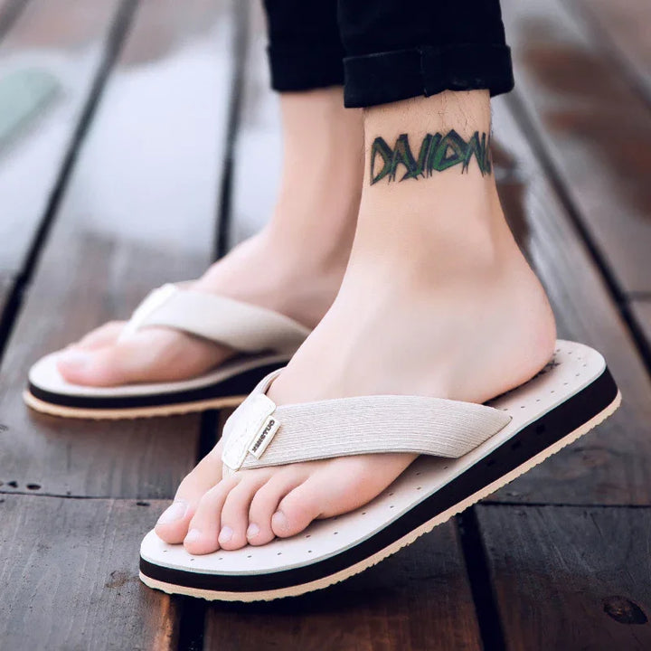 Close-up of feet wearing beige casual flip-flop sandals on wooden floor with ankle tattoo