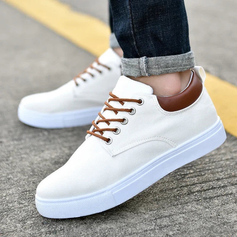 White canvas sneakers with brown leather collar and brown laces worn with rolled-up dark jeans on pavement