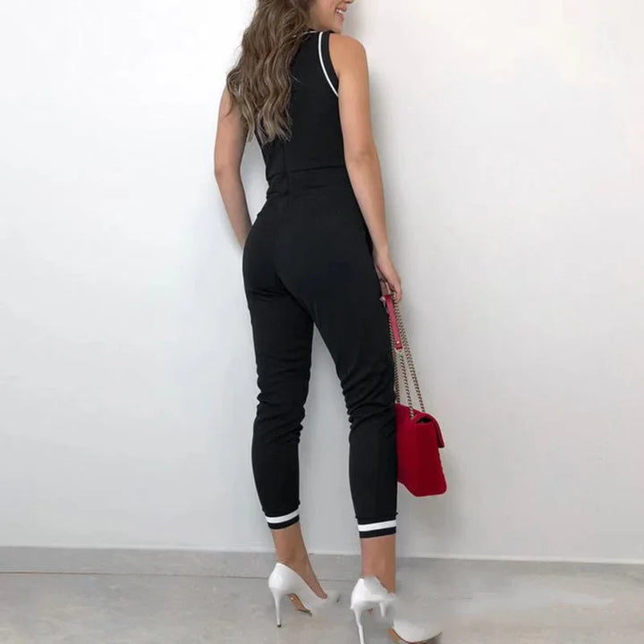 Woman wearing black sleeveless jumpsuit with white stripes, white high heels, and holding red handbag