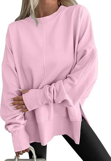 Woman wearing oversized light pink sweatshirt with raglan sleeves and side slits, paired with black leggings