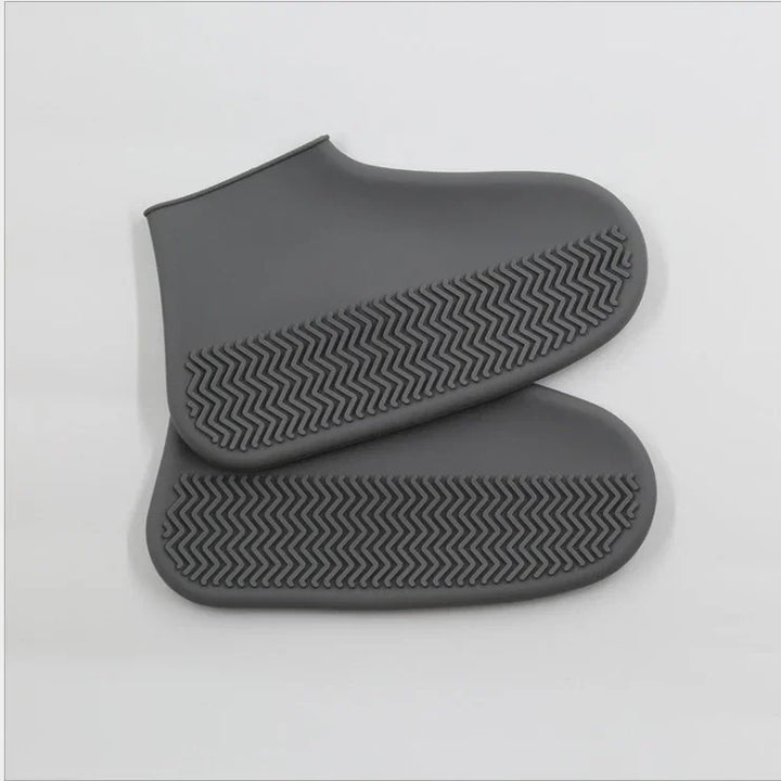 Pair of gray silicone shoe covers with non-slip zigzag soles on white background