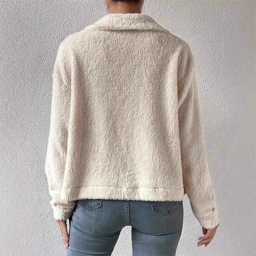 Back view of person wearing light beige fluffy fleece jacket with blue jeans against a textured wall