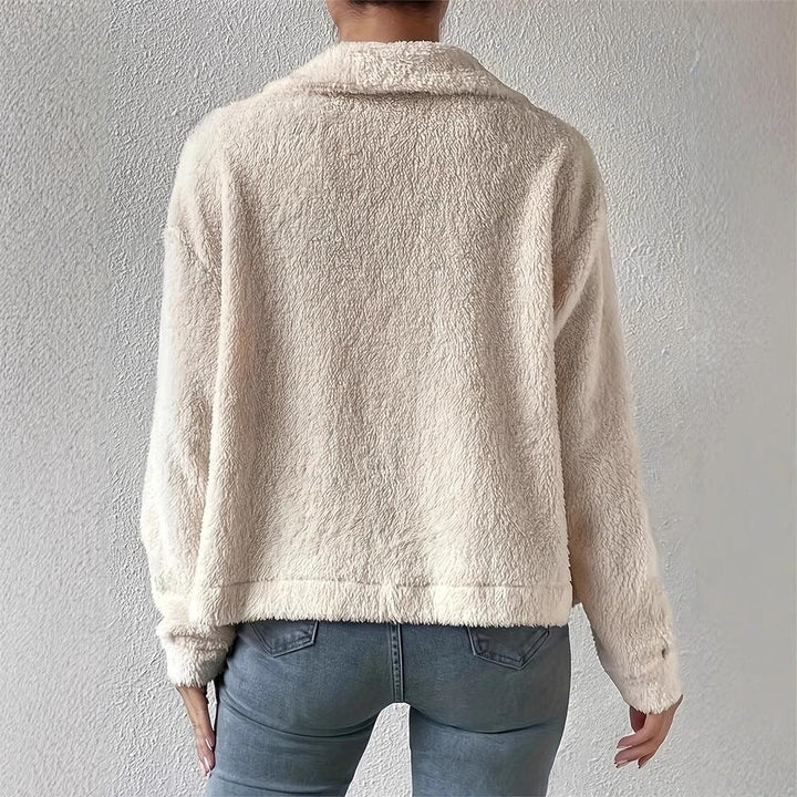 Back view of person wearing light beige fluffy fleece jacket with blue jeans against a textured wall