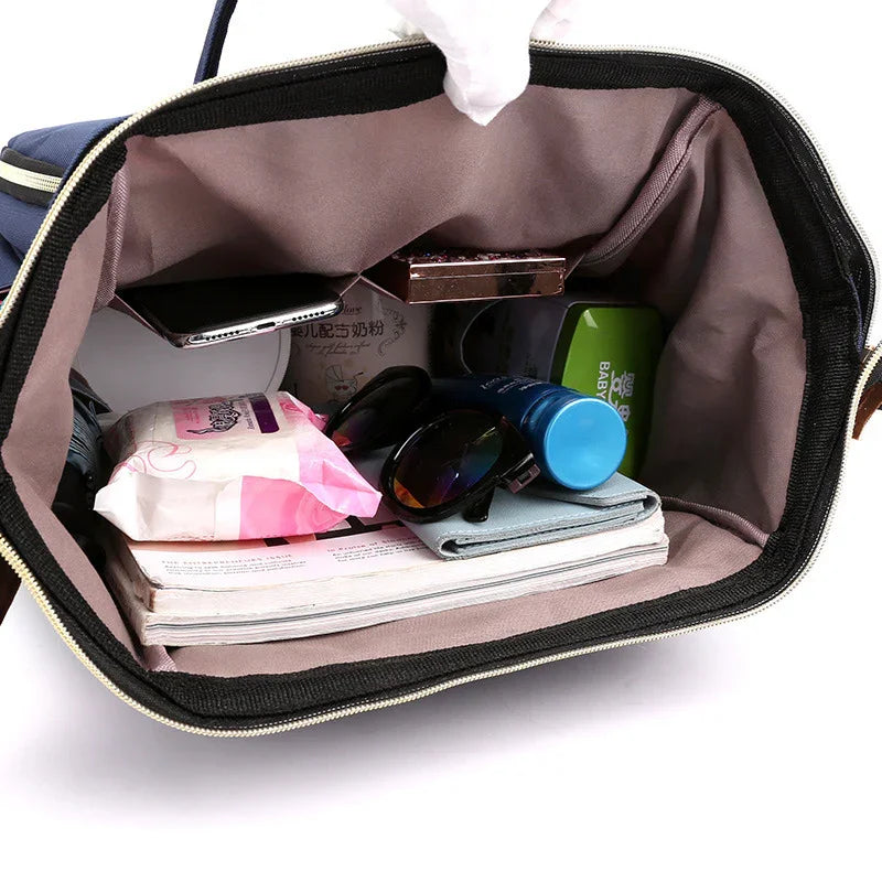 Interior view of open black bag with sunglasses, phone, lotion, tissues, wallet, and books inside