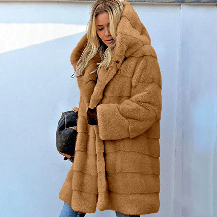 Blonde woman wearing a luxurious tan fur coat with hood and blue jeans against white wall
