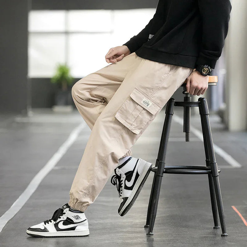 Person wearing beige cargo jogger pants and black white sneakers sitting on black stool in modern indoor space