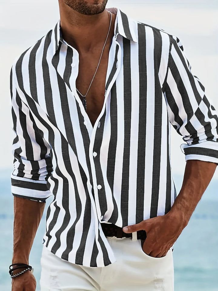 Man wearing black and white vertical striped shirt with rolled sleeves and white pants near beach