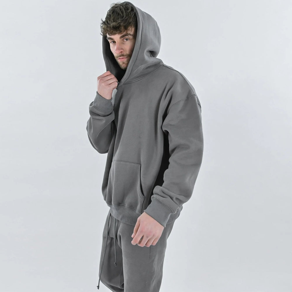 Young man wearing a gray hoodie and matching sweatpants posing against a plain light background