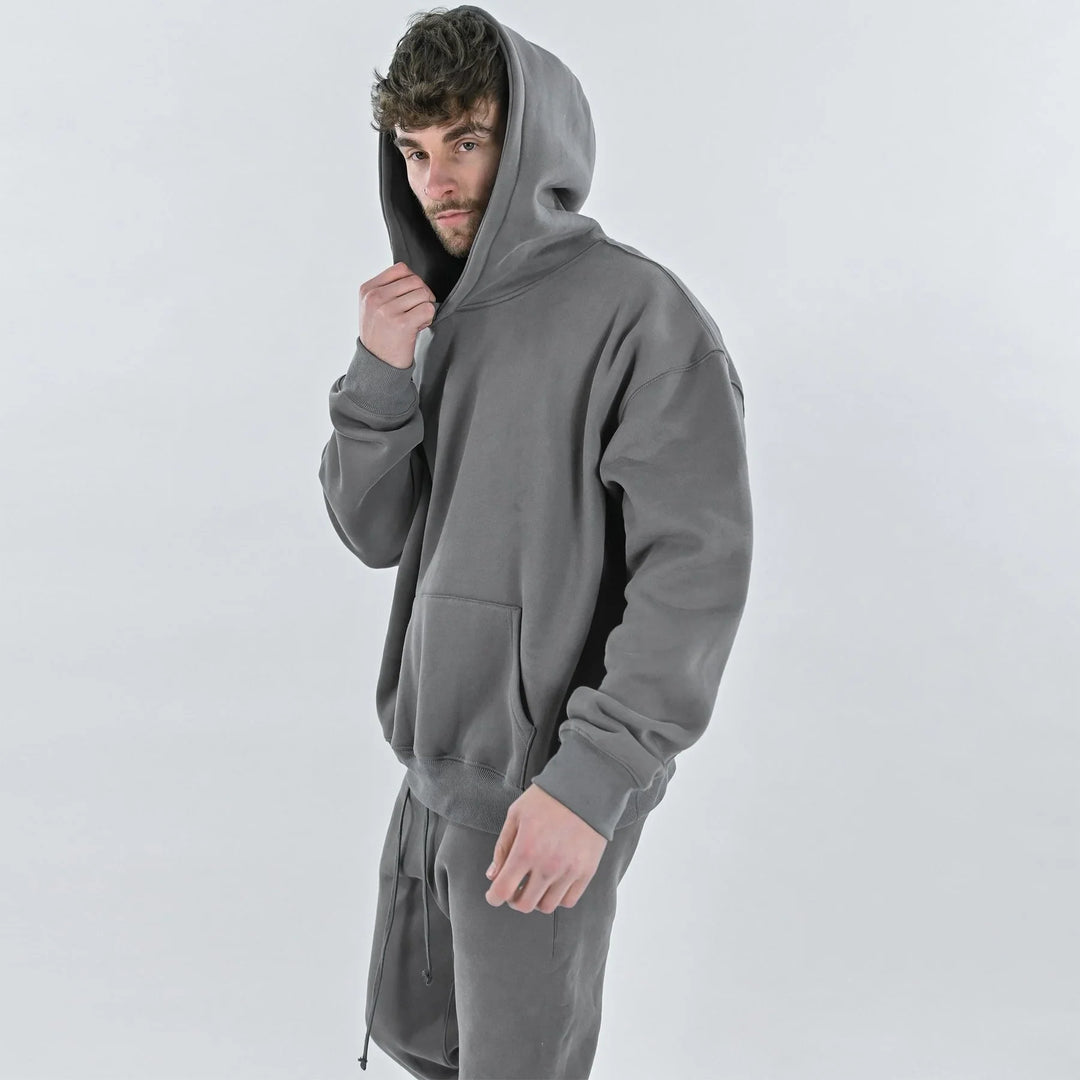 Young man wearing a gray hoodie and matching sweatpants posing against a plain light background