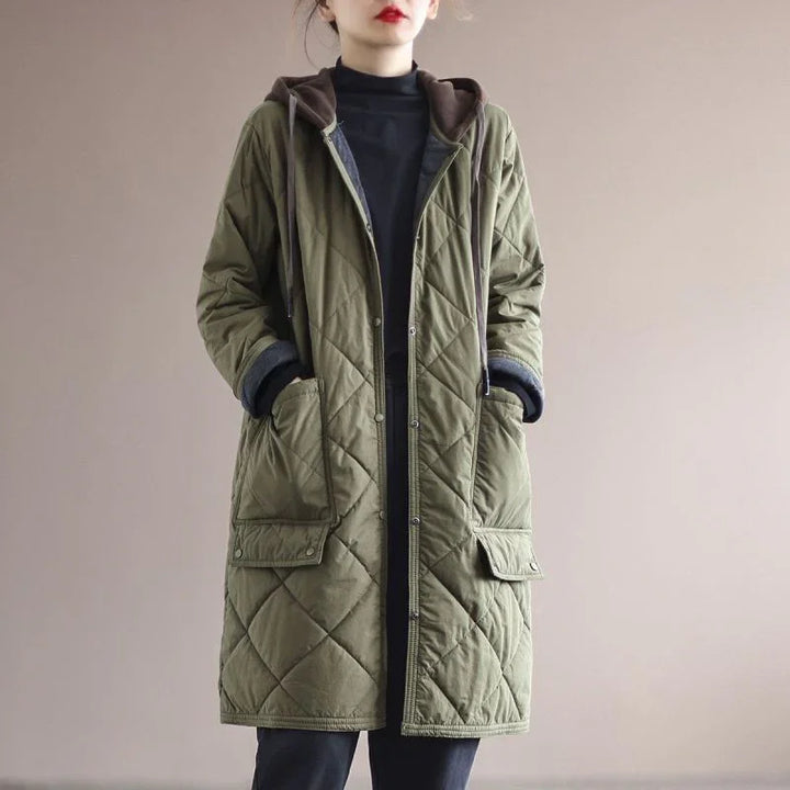 Woman wearing olive green quilted long coat with hood and front pockets over black turtleneck