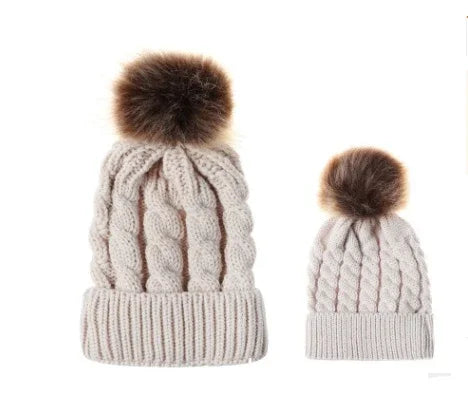 Two beige knit cable beanies with brown faux fur pom poms, one large and one small, isolated on white