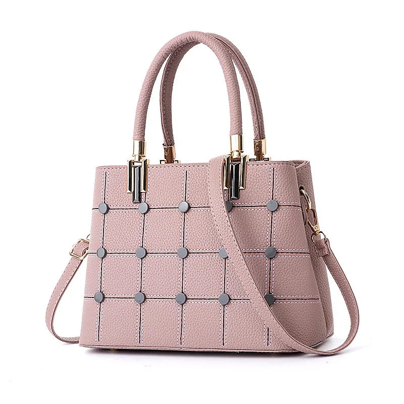 Pink textured leather handbag with grid pattern, metal studs, dual handles, and detachable shoulder strap