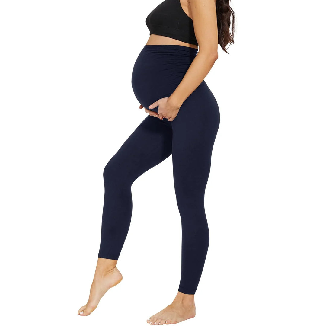 Pregnant woman wearing black maternity leggings and black sports bra on white background