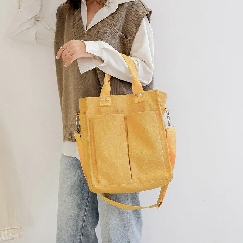 Woman wearing a beige vest and white shirt holding a yellow canvas tote bag with front pockets