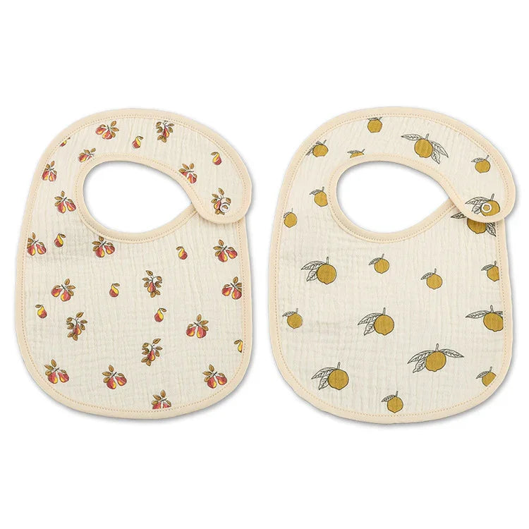 Two cream-colored baby bibs with snap closures, one with peach print, the other with orange print