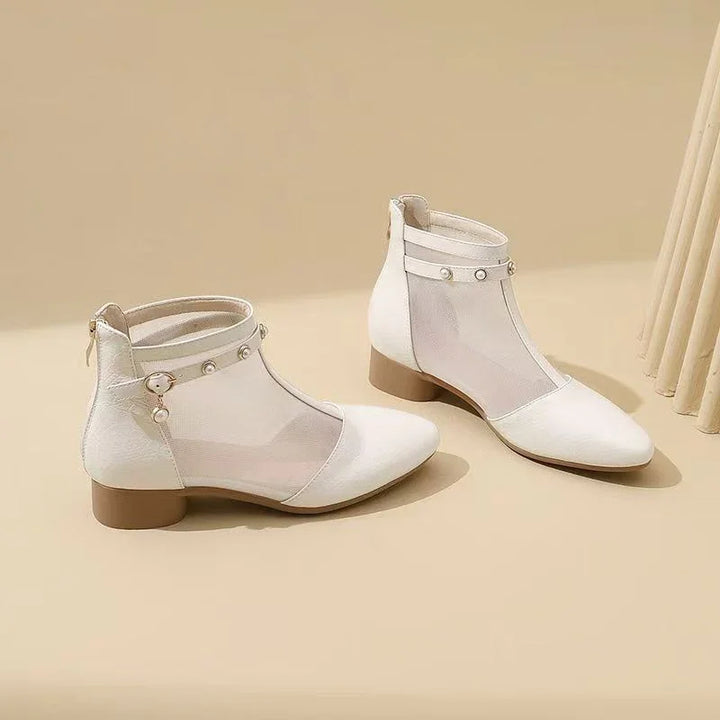 Pair of white mesh ankle boots with pearl and buckle accents on beige background
