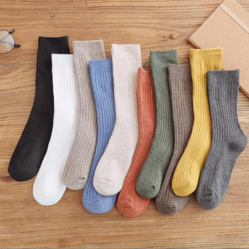 Nine pairs of ribbed socks in black, white, beige, blue, cream, orange, green, brown, yellow, and gray on wooden surface