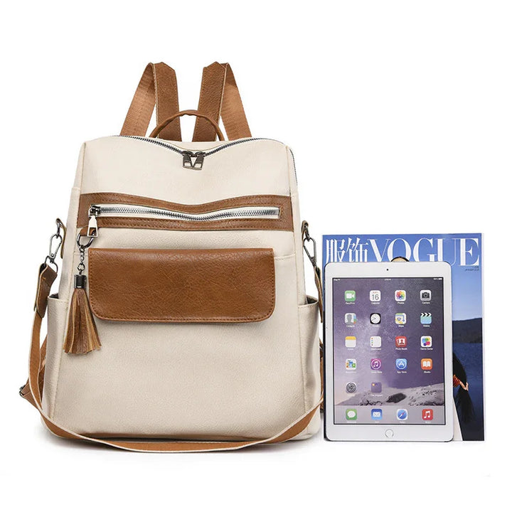 Beige and brown leather backpack with front pockets, tassel detail, tablet, and fashion magazine