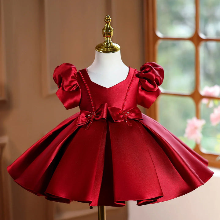 Elegant red satin baby dress with puff sleeves and bow embellishments on mannequin