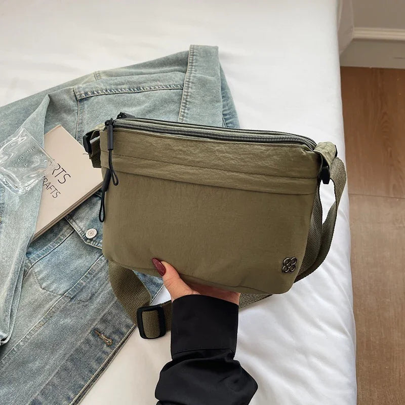 Hand holding olive green crossbody bag over a denim jacket on white bed with wooden floor