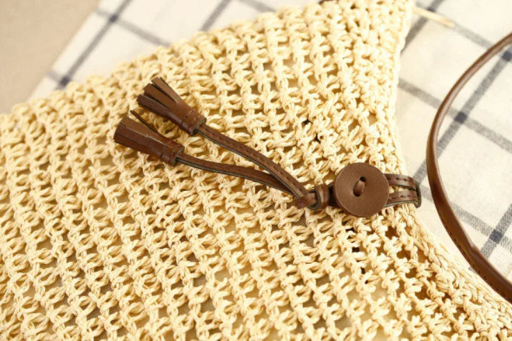 Close-up of a beige crochet bag with brown leather tassel and strap detail on a plaid fabric background