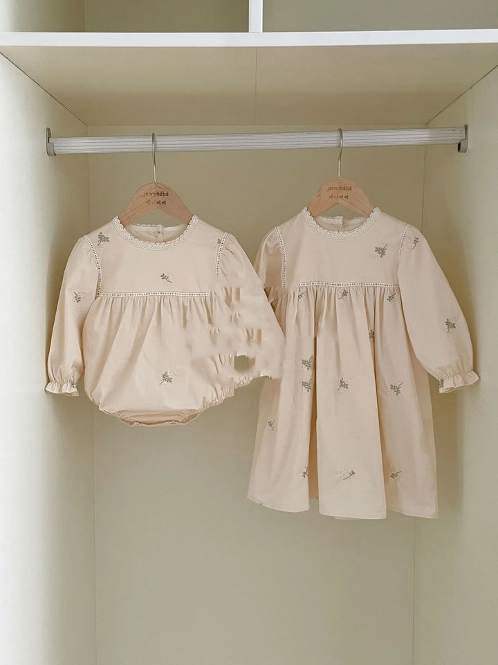 Cream-colored baby dress and romper with floral embroidery hanging on wooden hangers in closet