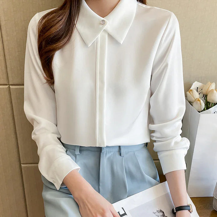 Woman wearing a white long-sleeve blouse with a jeweled collar button, paired with light blue high-waist trousers
