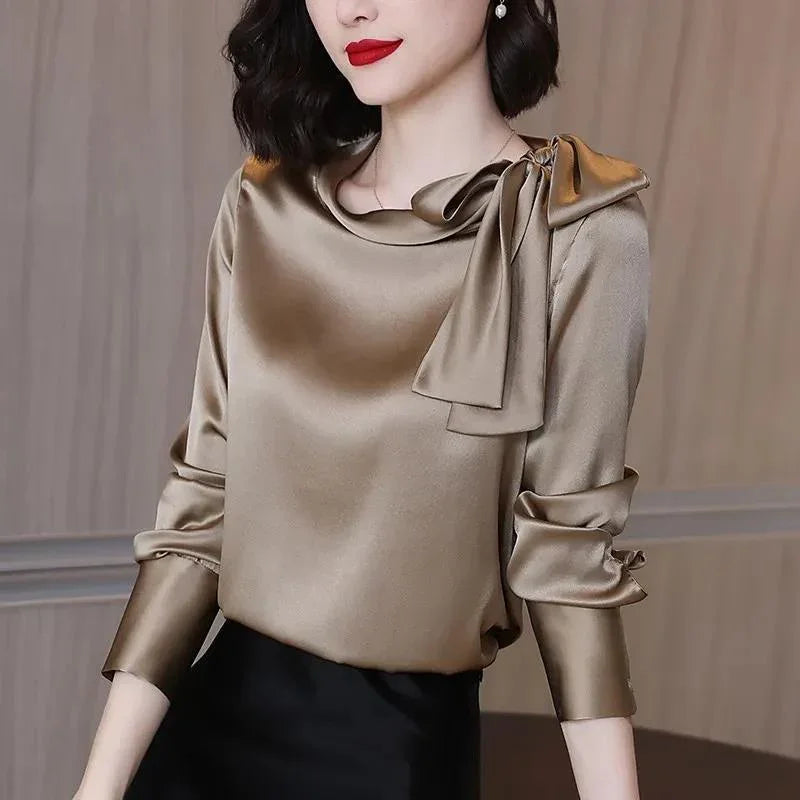 Woman wearing a shiny satin beige blouse with a large bow near the shoulder and red lipstick