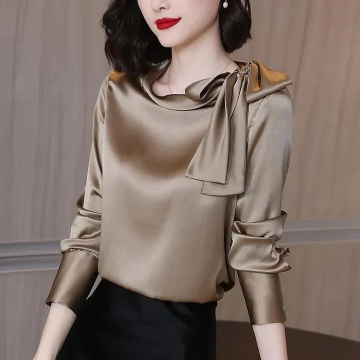 Woman wearing a shiny satin beige blouse with a large bow near the shoulder and red lipstick