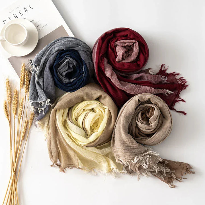 Rolled scarves in grey, navy, red, cream, and beige on white surface with cup, magazine, and wheat stalks