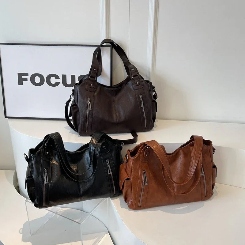 Three leather handbags in black, brown, and dark brown colors on white shelves with 'FOCUS' sign