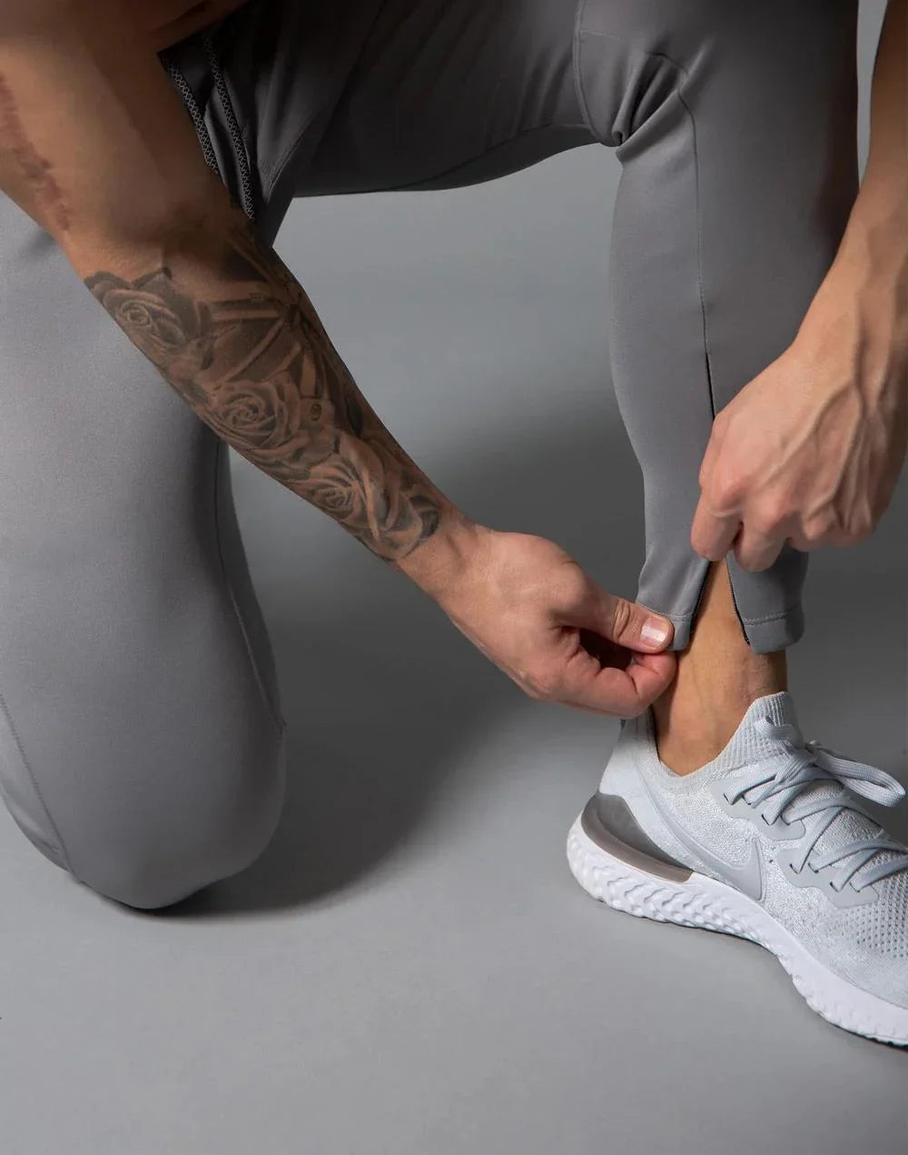 Close-up of person adjusting grey athletic leggings and wearing light grey Nike running shoes on grey floor