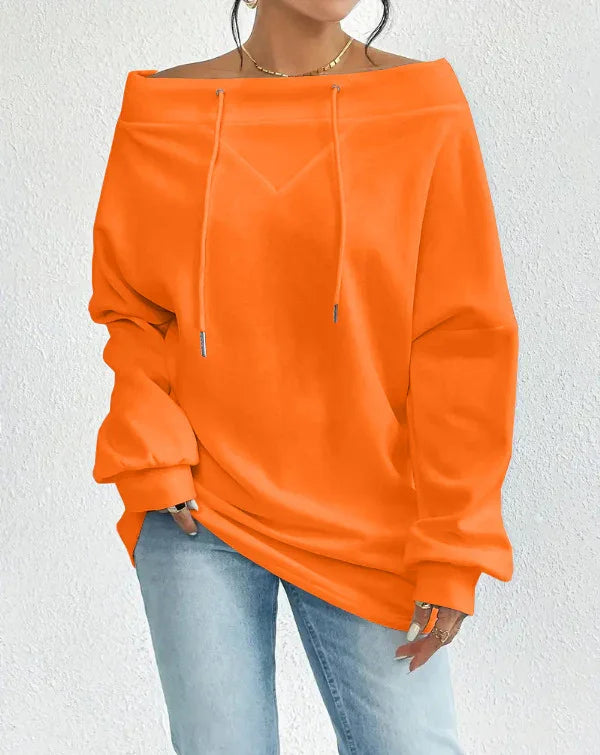 Woman wearing oversized off-shoulder bright orange sweatshirt with drawstrings and light blue jeans