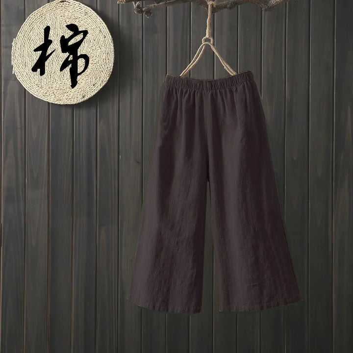 Dark wide-leg cotton pants hanging on rope against dark wooden wall with woven circle decor