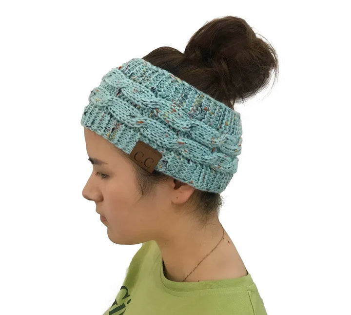 Woman wearing blue knitted cable headband with CC leather patch and bun hairstyle