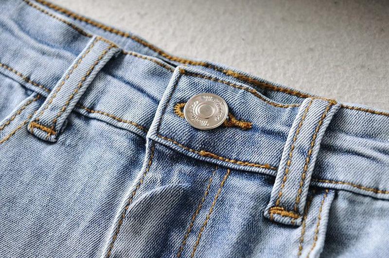 Close-up of light blue denim jeans with silver button and yellow stitching details