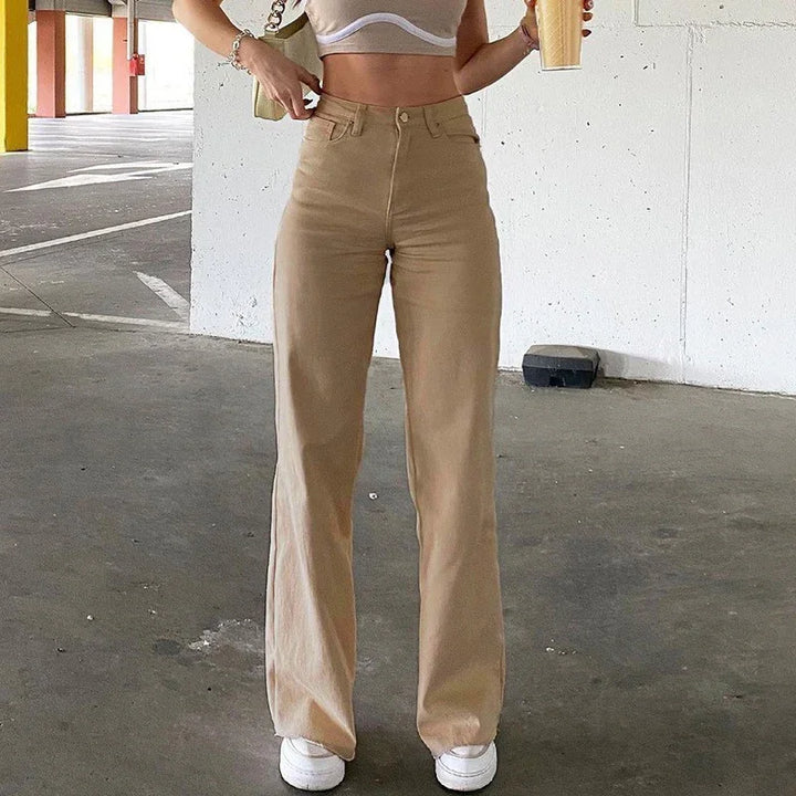 Woman wearing high-waisted beige wide-leg pants and white crop top, holding a drink in parking garage