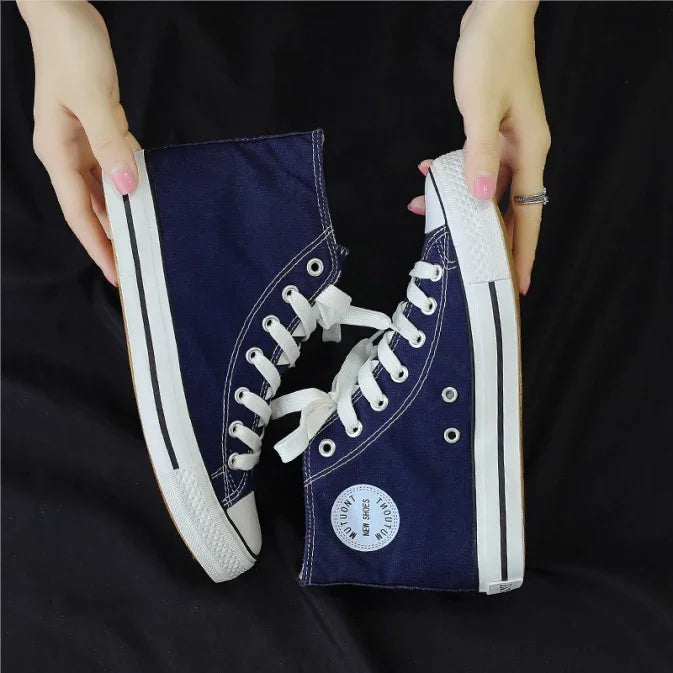 Hands holding navy blue high-top canvas sneakers with white laces and rubber soles on black background