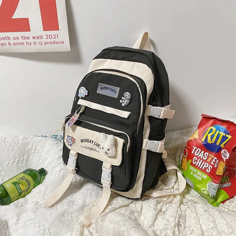 Black and beige Monday Lucy backpack with pins, next to Ritz Toasted Chips and a green bottle on a fabric surface