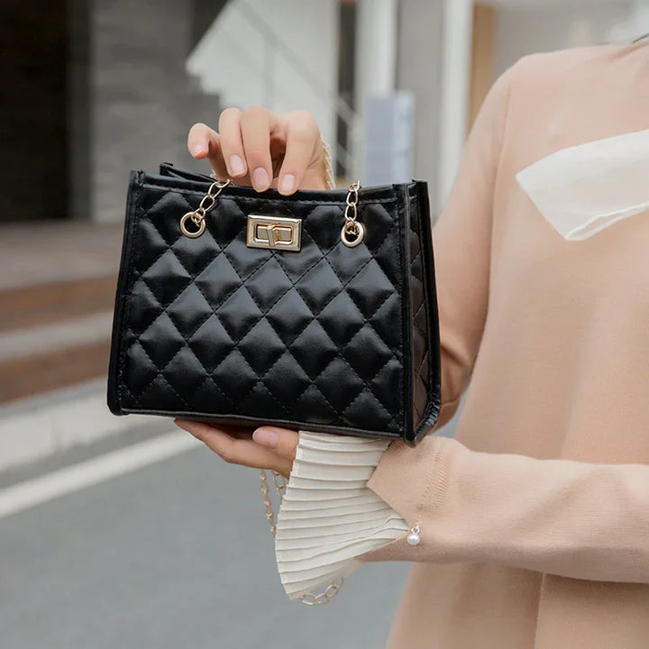 Woman holding black quilted leather handbag with gold chain strap and clasp outdoors