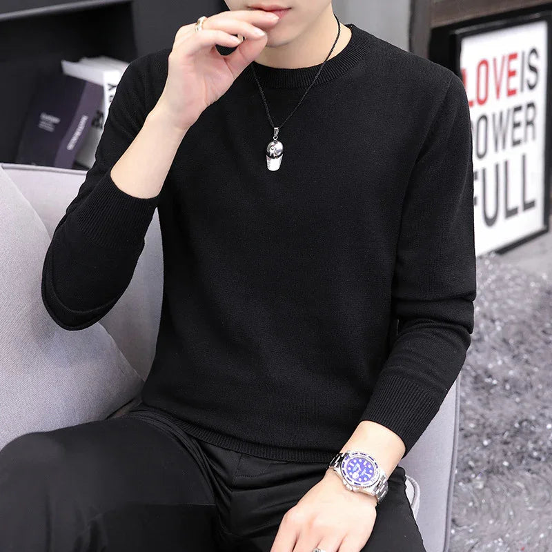 Man in black sweater and pants wearing silver wristwatch and pendant necklace sitting on gray sofa