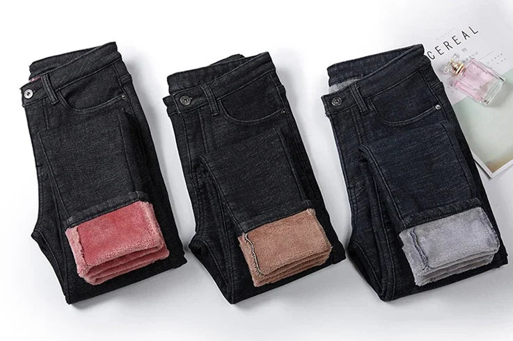 Three pairs of folded black jeans with pink, brown, and gray fleece lining on a white background with a magazine and perfume