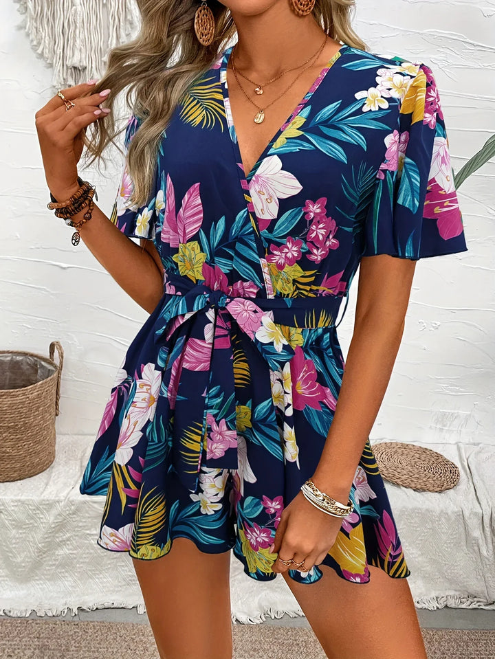 Woman wearing navy blue tropical floral print romper with short sleeves and waist tie