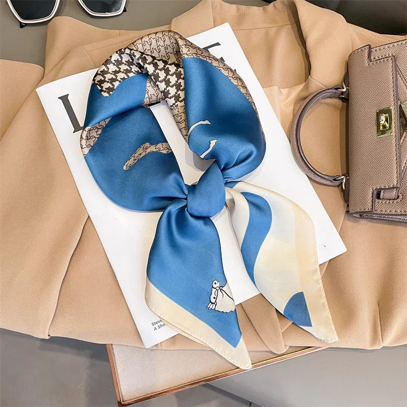 Blue and beige silk scarf with houndstooth pattern on tan coat beside brown handbag and sunglasses