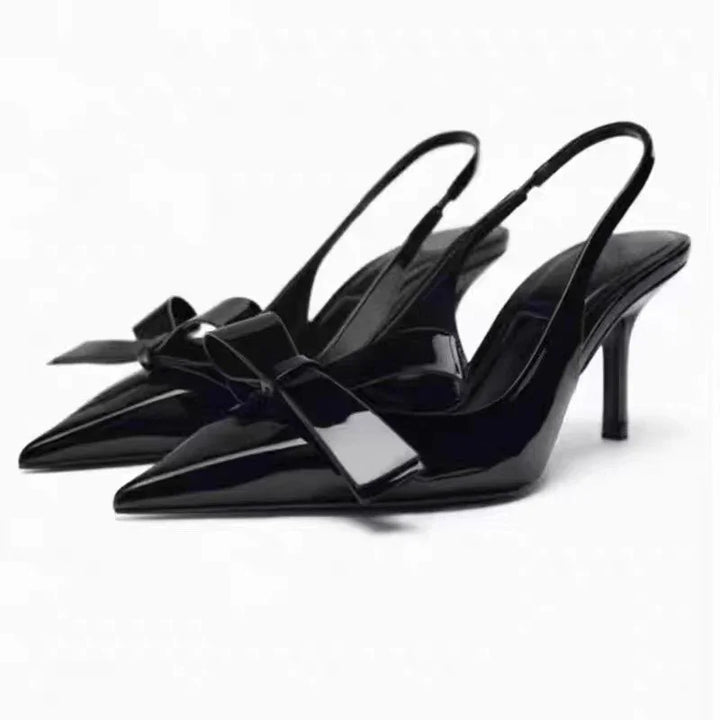 Black patent leather slingback high heels with a pointed toe and bow detail on white background