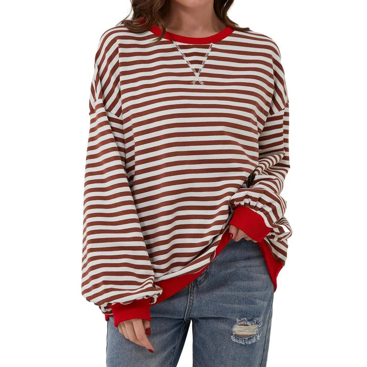 Woman wearing oversized brown and white striped sweatshirt with red cuffs and collar, paired with ripped jeans