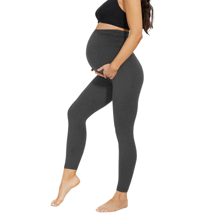 Pregnant woman in black sports bra and dark gray maternity leggings on white background