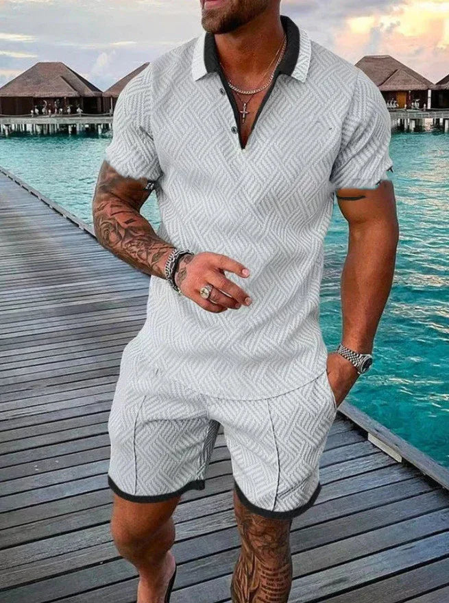 Man wearing white patterned polo shirt and shorts standing on wooden pier by tropical overwater bungalows