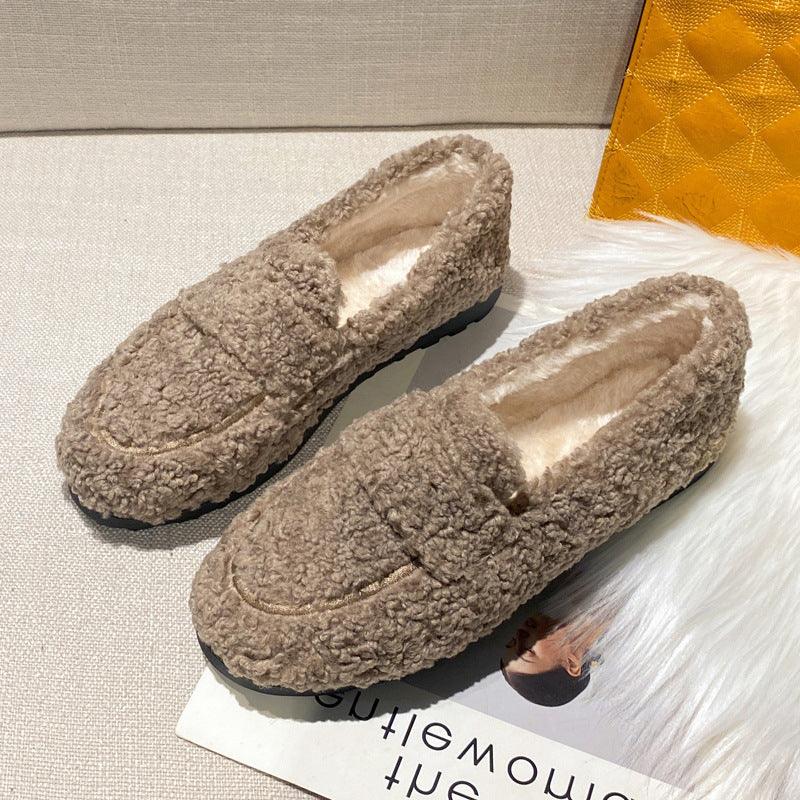 Pair of cozy brown fuzzy loafers with black soles on a beige surface and white fur rug