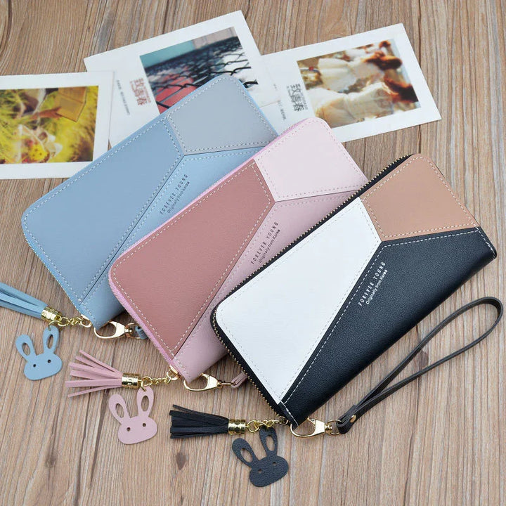 Three color-blocked zip wallets with tassel and bunny charm on wooden surface and photos